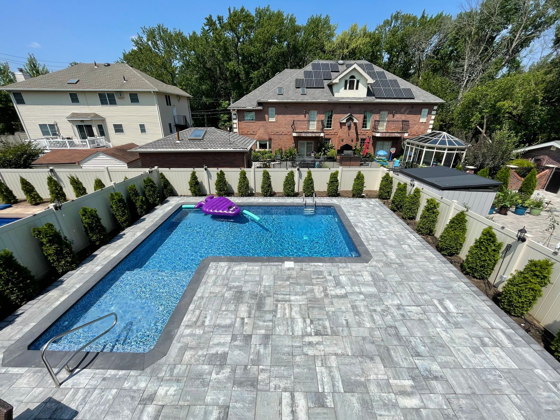 Backyard with rectangular pool, gray paver patio, white retaining walls, and a house in the background