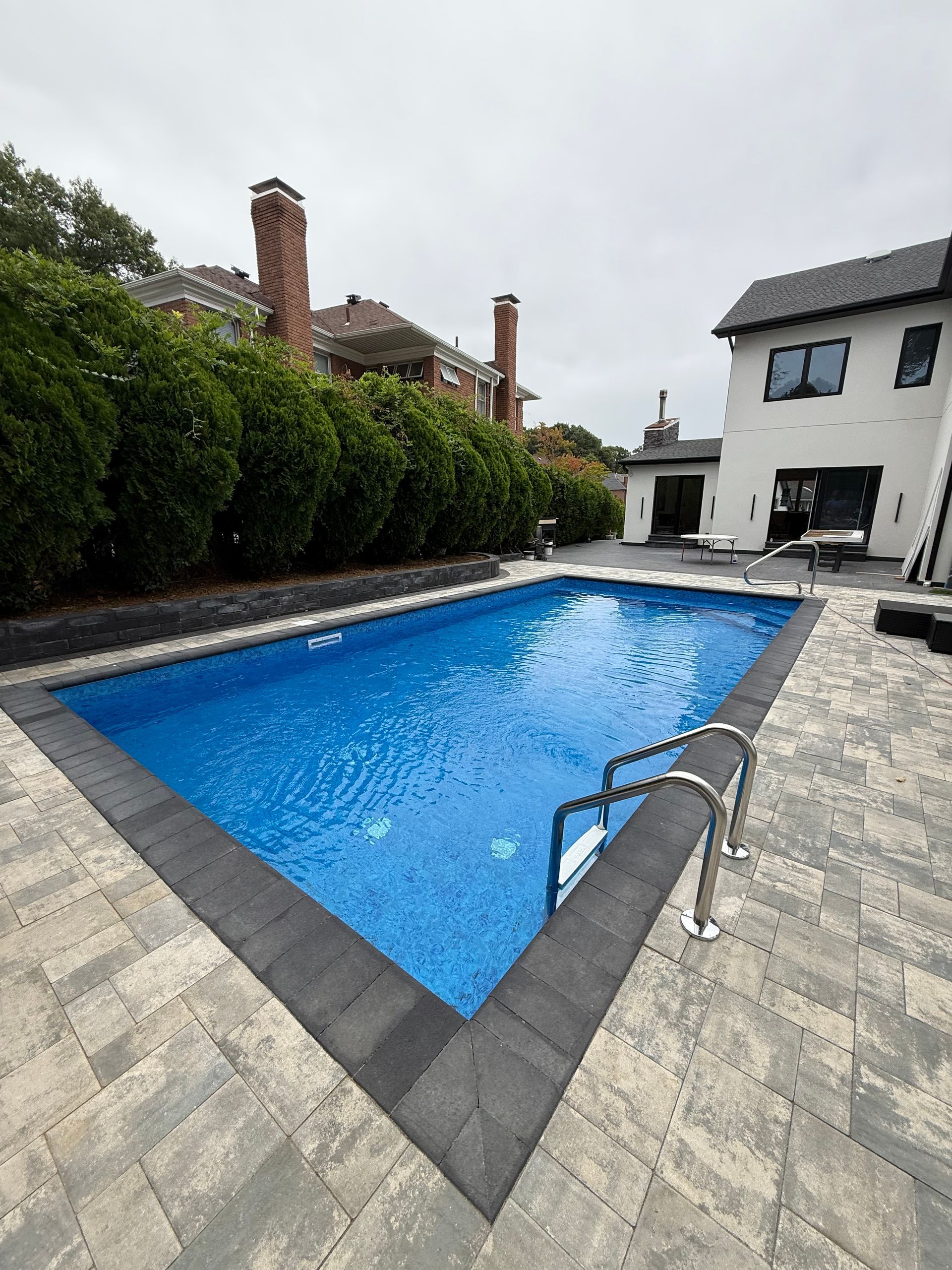 Backyard swimming pool with blue water beside a house and patio, viewed on an overcast day