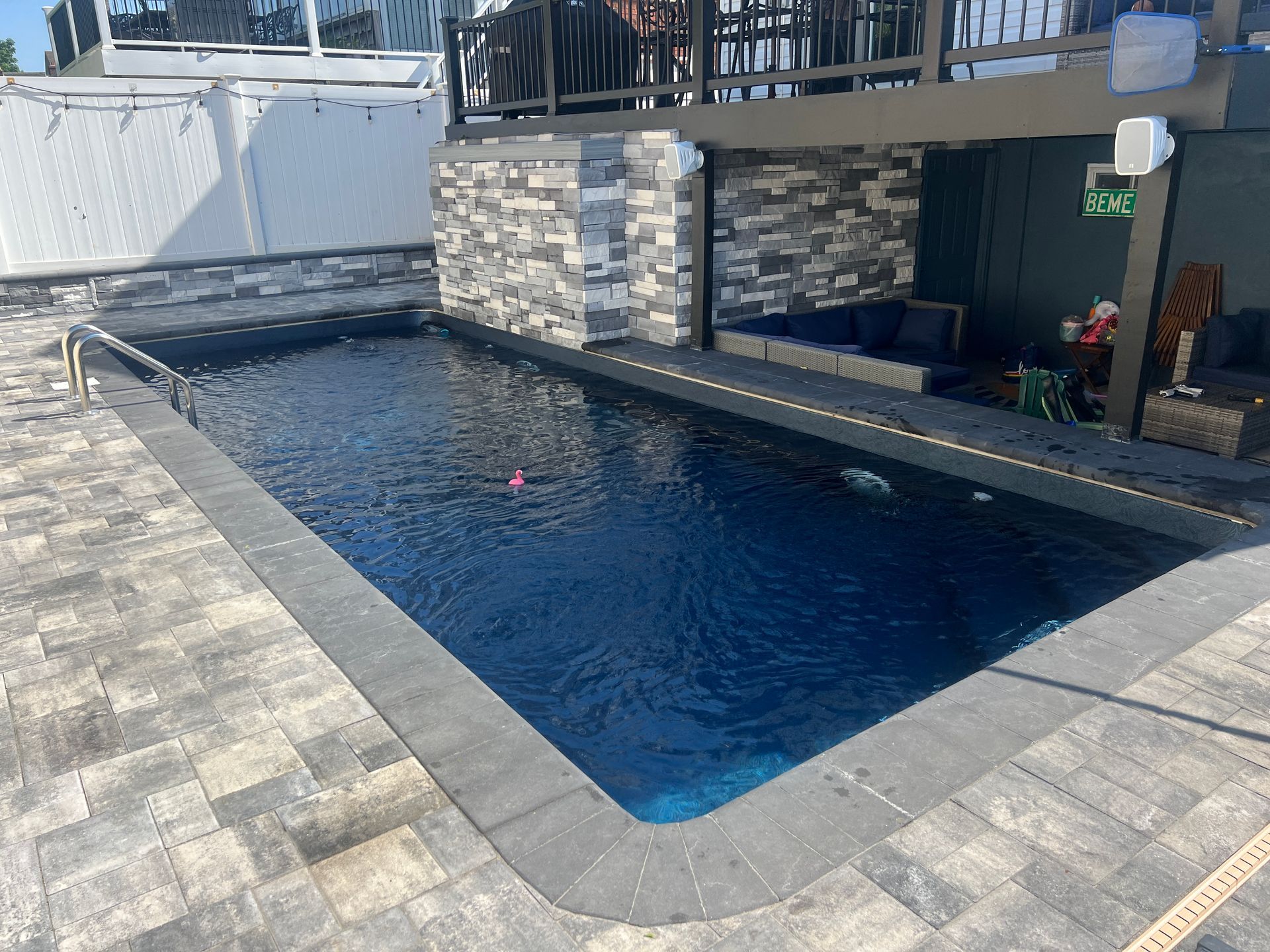 Rectangular outdoor swimming pool with dark blue water beside a stone-tiled patio and deck area