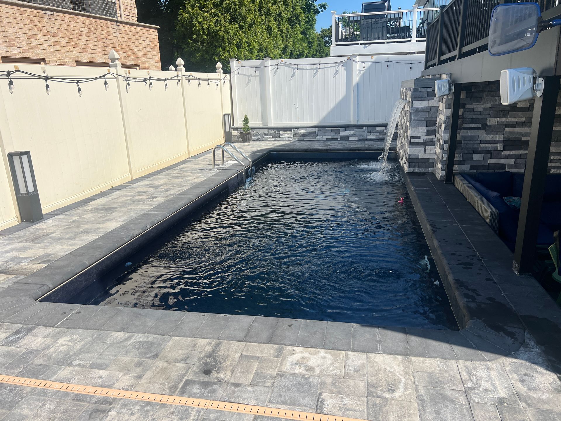 Rectangular outdoor swimming pool with dark water, surrounded by stone decking and white walls