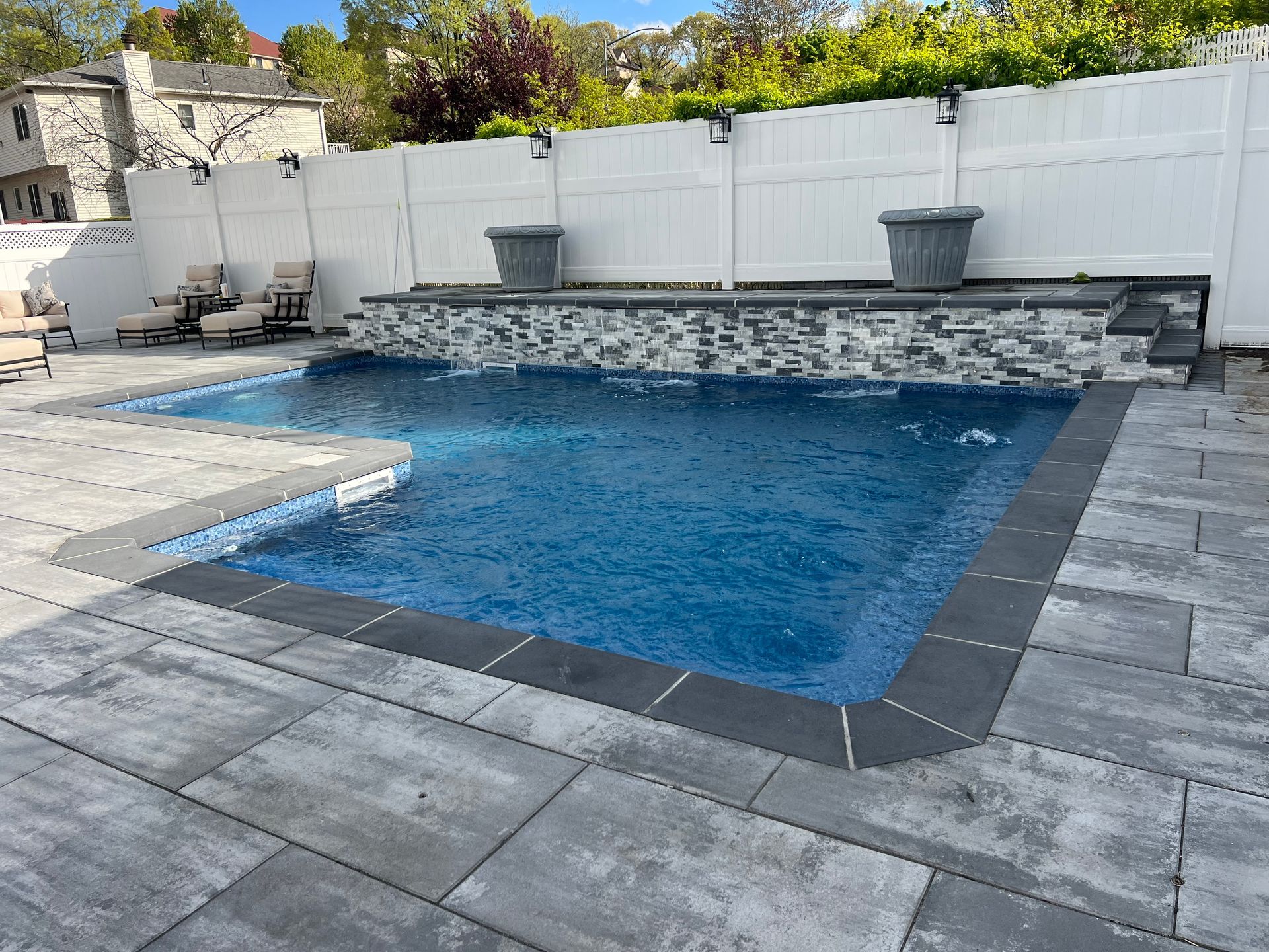 Backyard swimming pool with stone patio, white fence, and raised spa wall