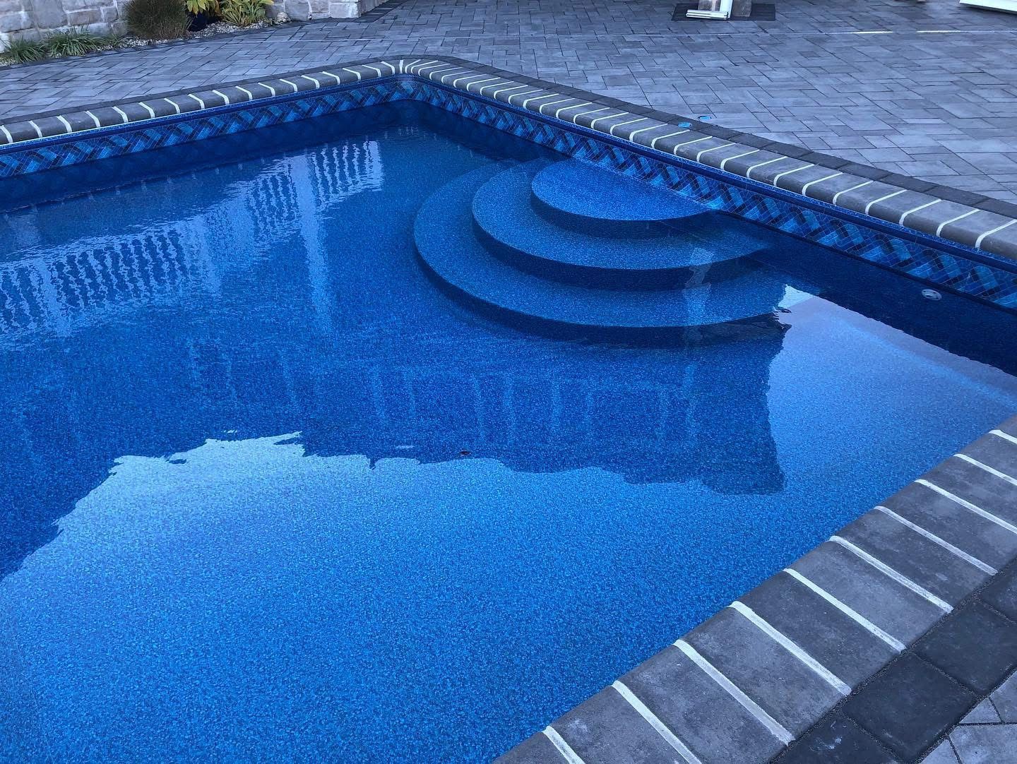 Blue swimming pool with curved steps and a dark stone deck around the edge