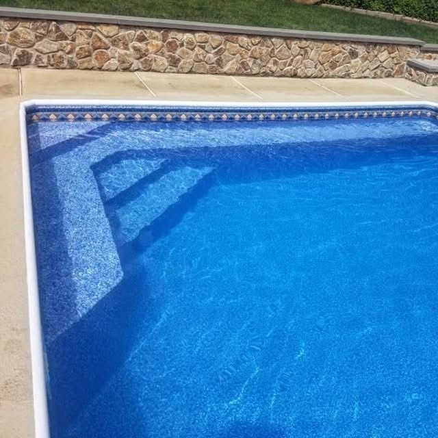Blue swimming pool with sunlit water, stone border, and shallow steps in the corner