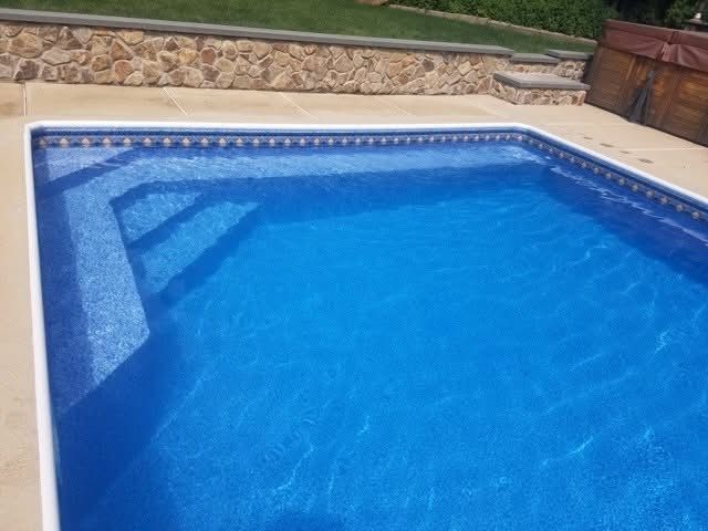 Blue backyard swimming pool beside a stone patio and grassy lawn