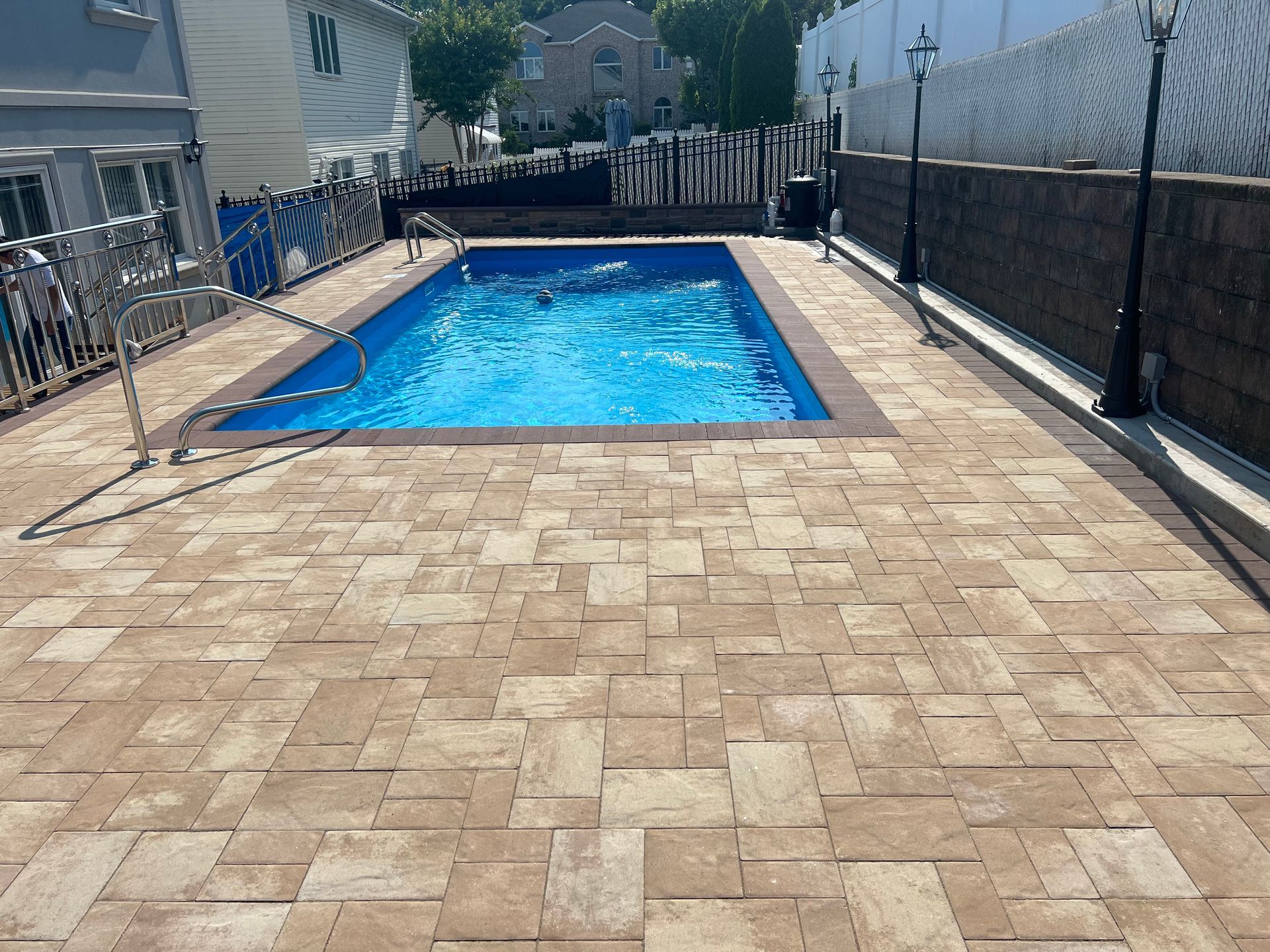 Rectangular backyard swimming pool beside a stone patio, with a hose and fencing on both sides