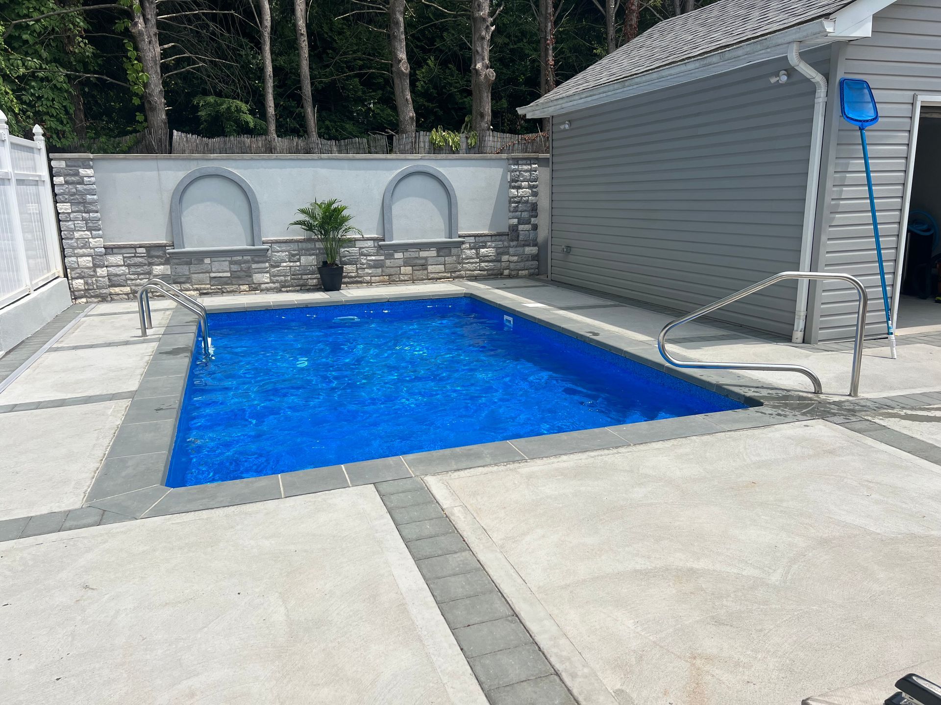 Blue backyard swimming pool beside a gray shed and white patio wall, with lounge chairs nearby