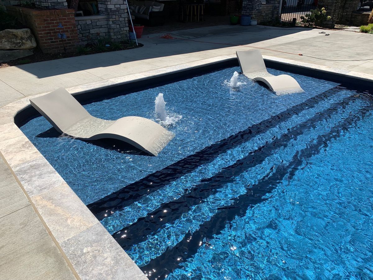 Outdoor pool with a blue mosaic interior and two curved white lounge chairs in shallow water