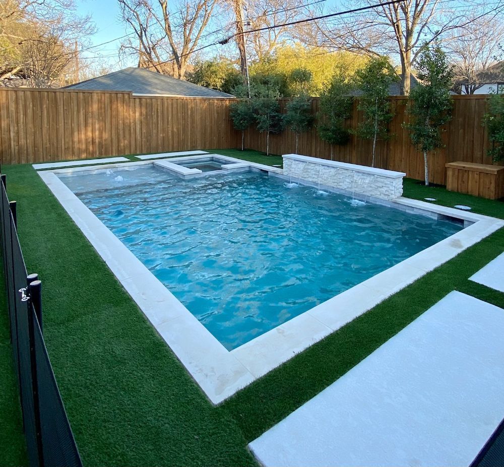 Backyard rectangular pool with blue water, white coping, and green turf beside a wooden fence