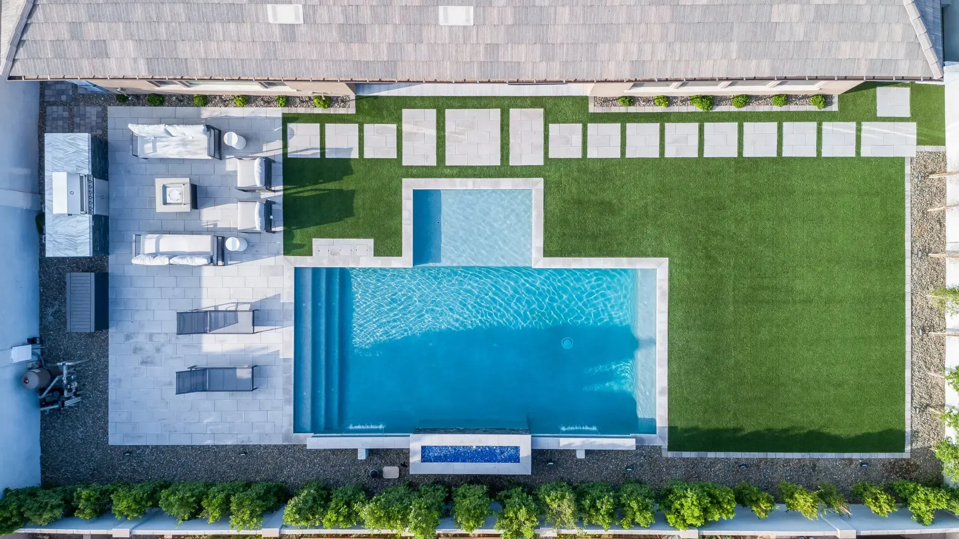 Aerial view of a backyard with a rectangular swimming pool, stone patio, and green lawn.