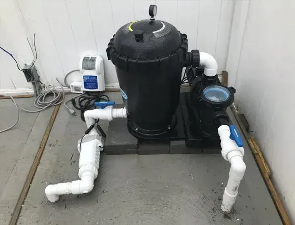 Black pool pump and filter system with white PVC pipes on a concrete floor indoors