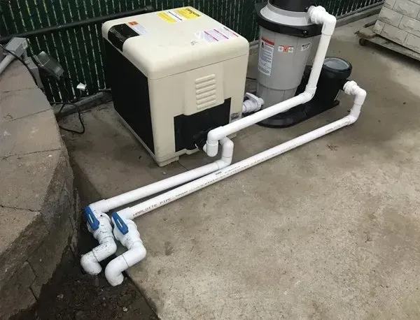 Pool pump and filter equipment with white PVC piping on a concrete patio outdoors
