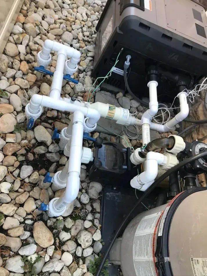 White PVC pool plumbing and pump equipment on gravel beside a black filter unit.