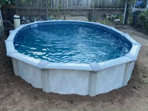 Above-ground pool with blue water in a backyard, surrounded by white panels and a fence