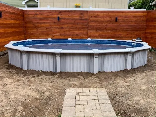 Round above-ground pool in a dirt yard with a wooden fence and paver path leading to it