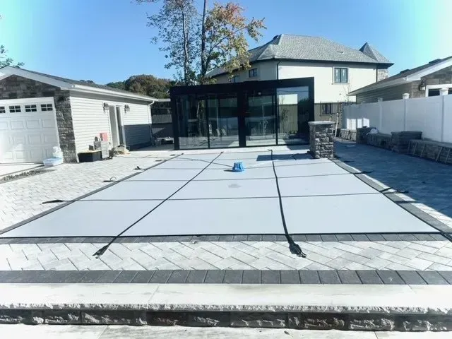 Backyard with a covered pool being prepared, surrounded by a paved patio and house walls