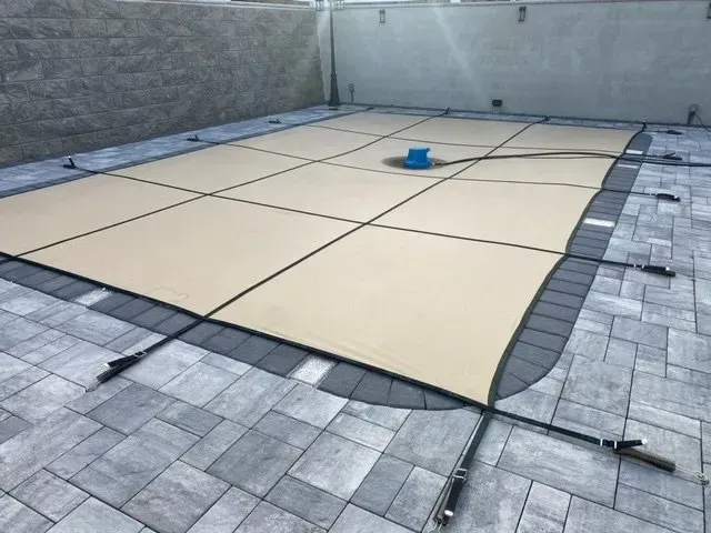 Covered backyard pool with beige safety cover and a blue bucket-like object in the center