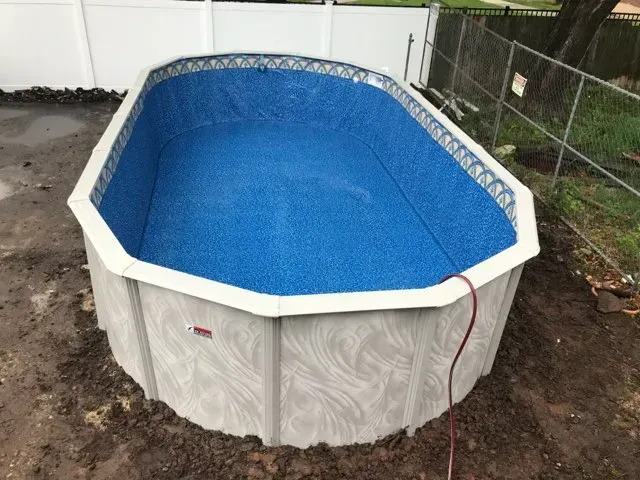 Above-ground octagonal pool with blue liner in a muddy backyard