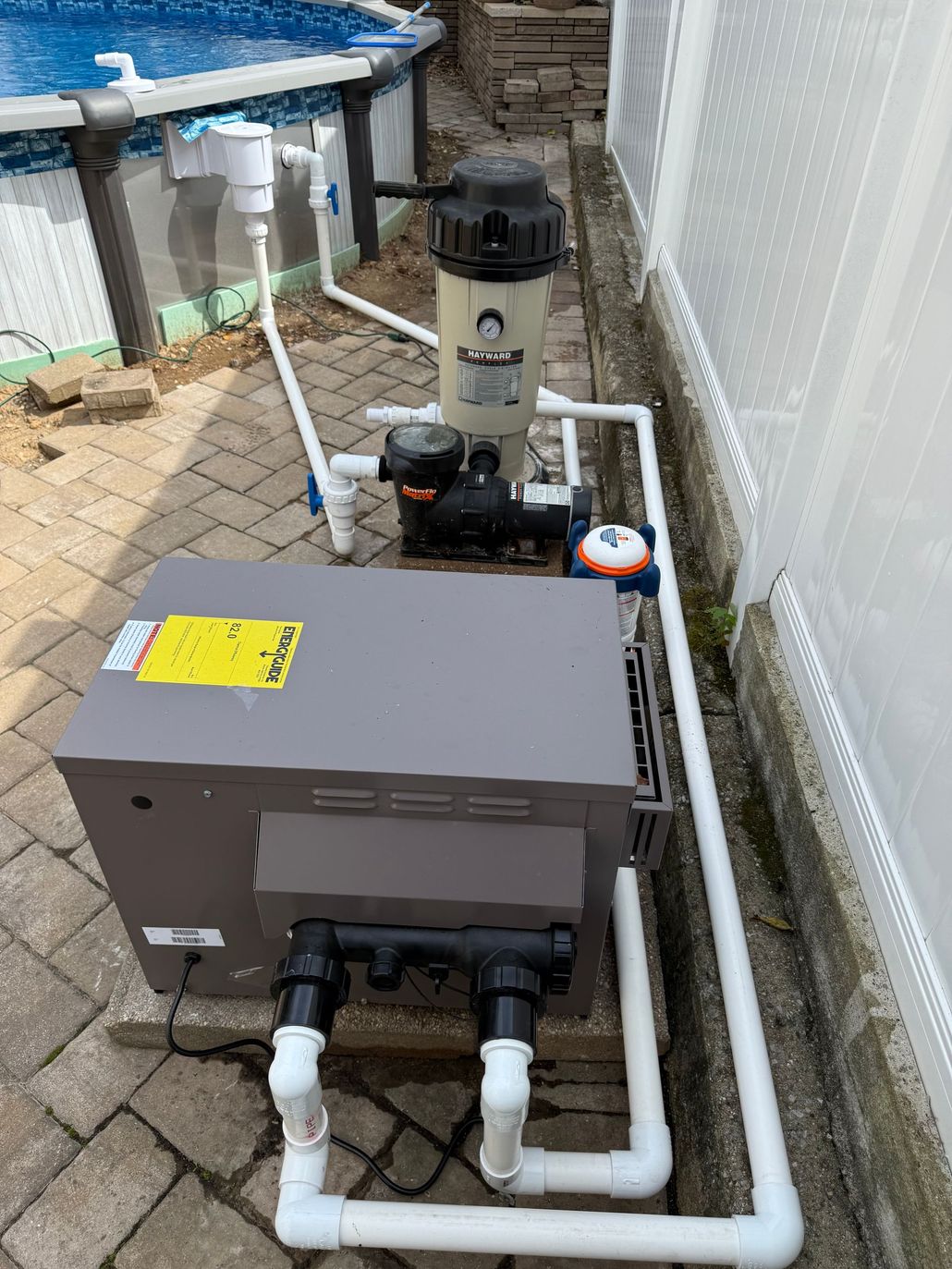 Pool equipment with gray control box, pipes, pump, and filter beside an above-ground pool.