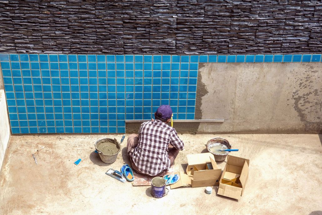 Person painting a wall blue beside a concrete floor with paint buckets and tools