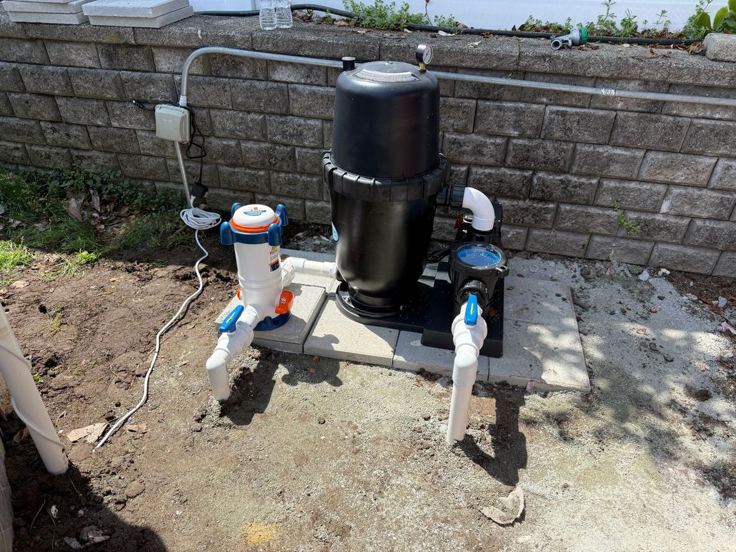 Outdoor water filtration system with black tank and white pipes beside a brick retaining wall