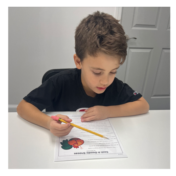 a young boy is sitting at a table writing on a piece of paper with a pencil