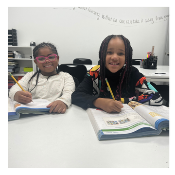 two young girls are sitting at a desk with books and pencils