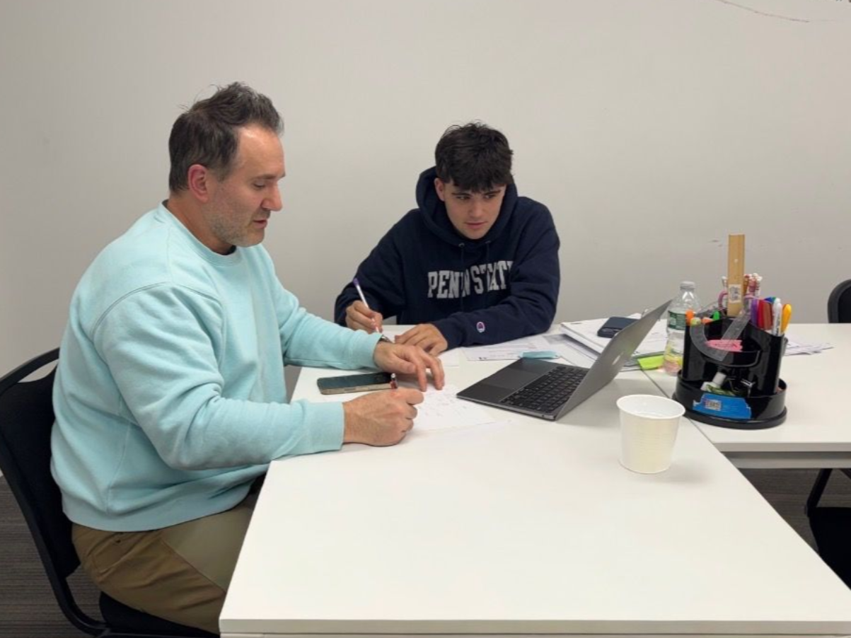 Two people sit at a white table in an office, working on documents together with a tablet present.