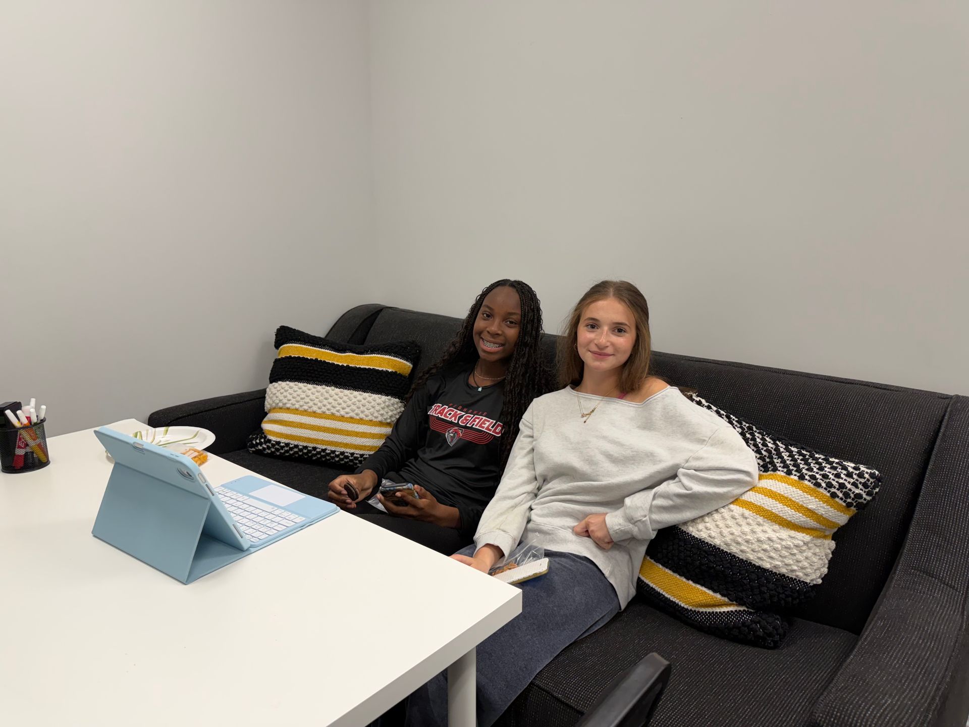 A person helps a young person seated at a table, both working on papers in a room.
