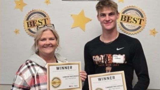 Two award winners holding plaques in front of a “Best” backdrop with gold stars