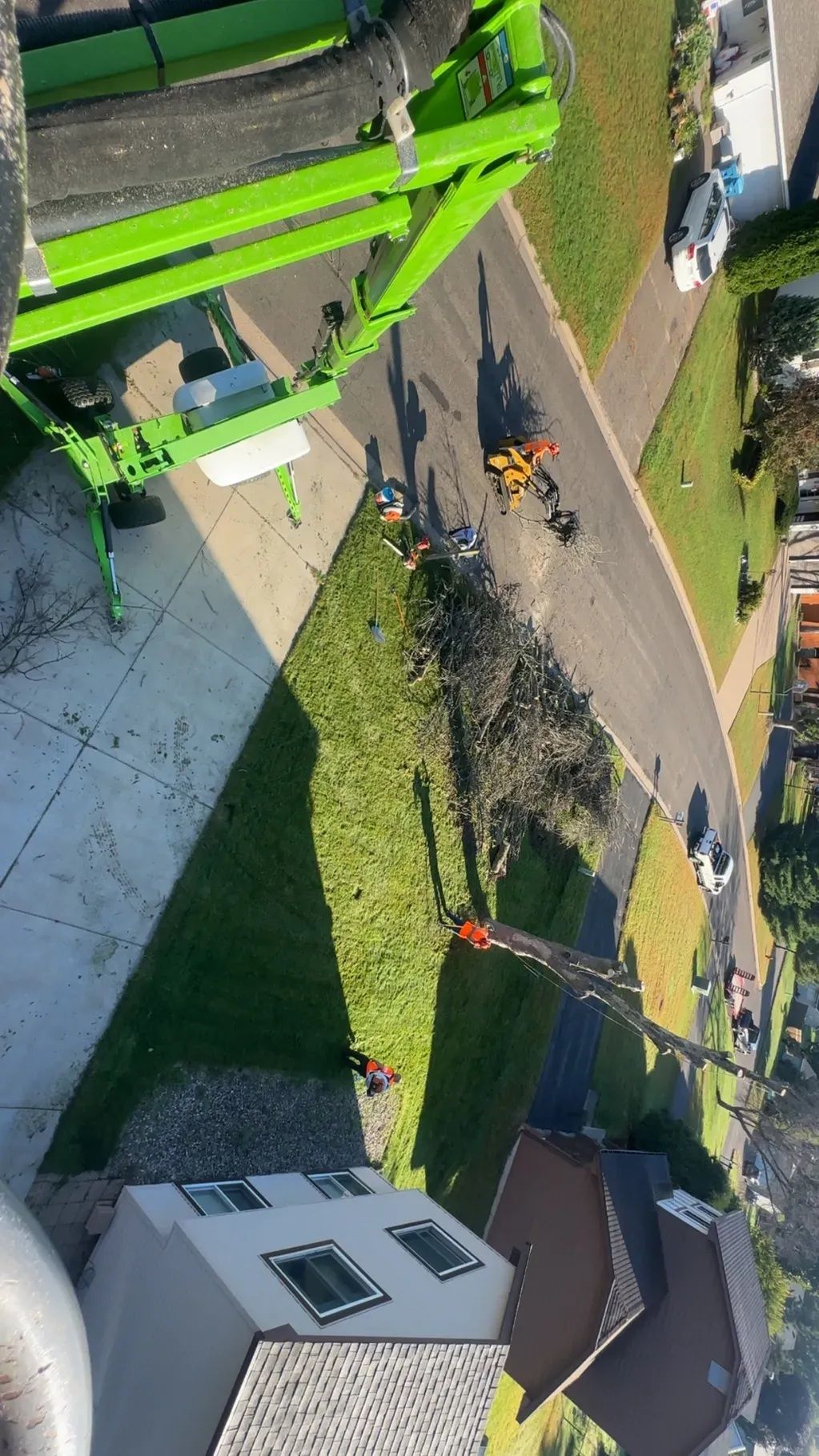 Aerial view of firefighters and a green ladder truck on a residential street with smoke or debris nearby.