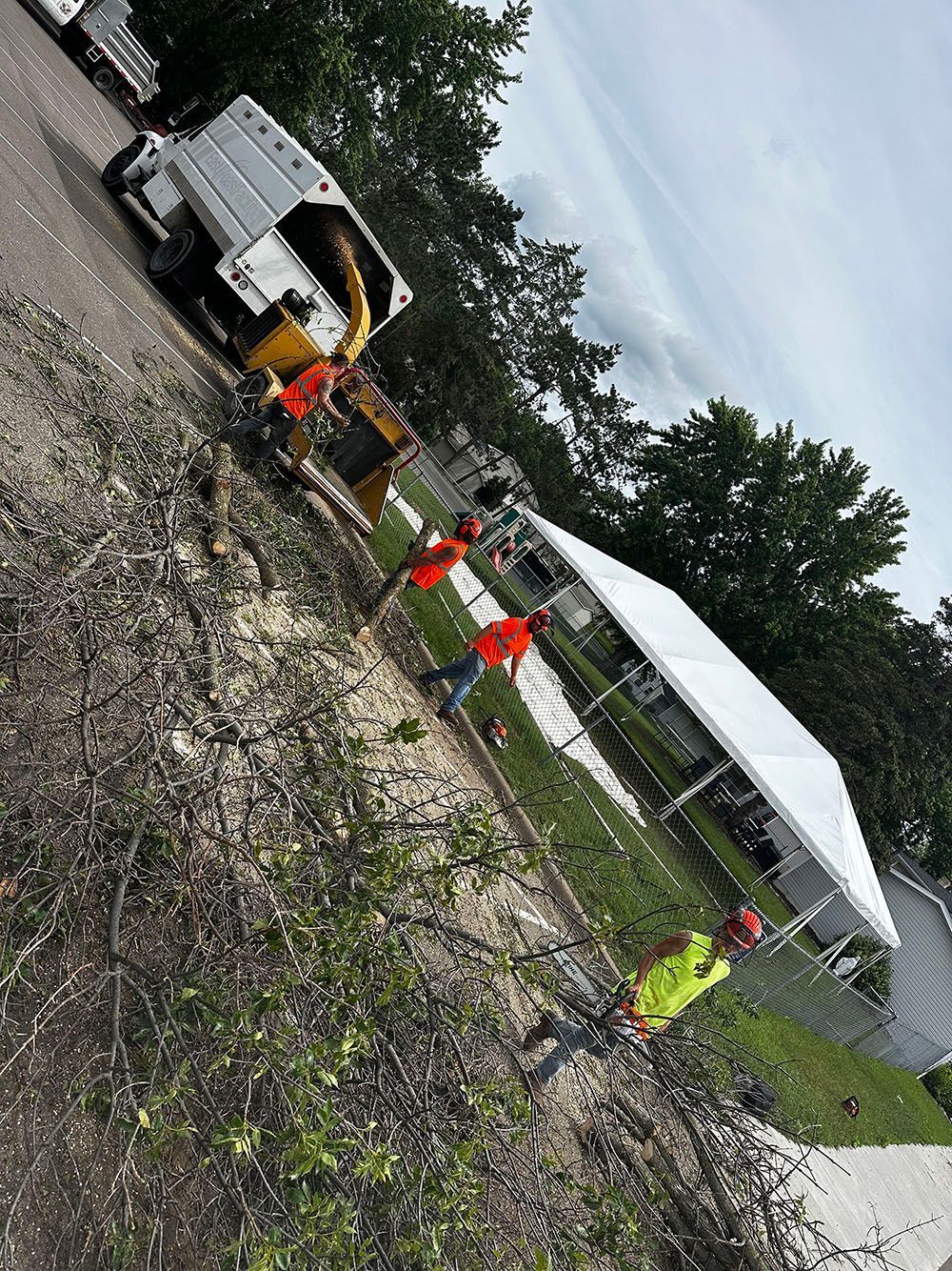 Workers in orange vests beside a white truck and equipment on a muddy roadside under a canopy