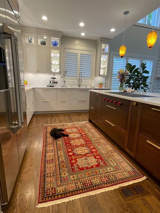 A cat is laying on a rug in a kitchen.