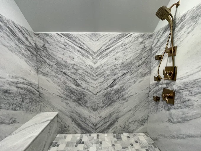 A bathroom with marble walls and a walk in shower with a bench.