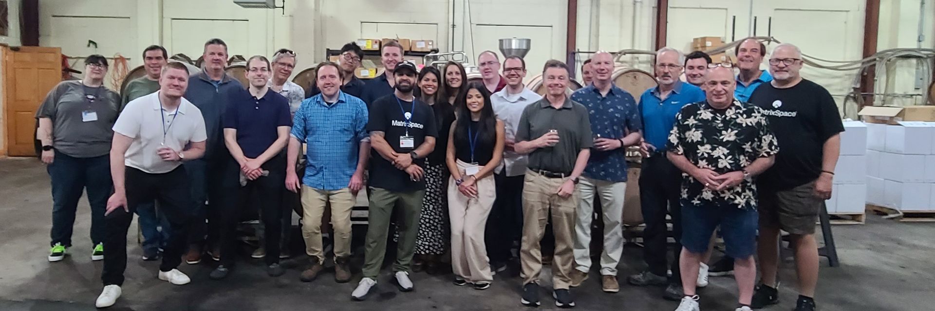 Group of people standing together indoors, posing for a photo in front of shelves and a white wall.