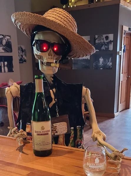 Skeleton in a straw hat at a bar table with glowing red eyes, bottles, and a glass.