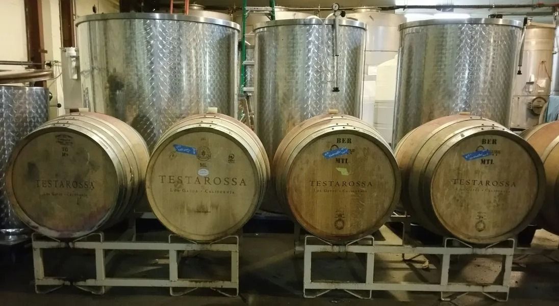 Rows of large metal industrial tanks and barrels in a warehouse or storage facility.
