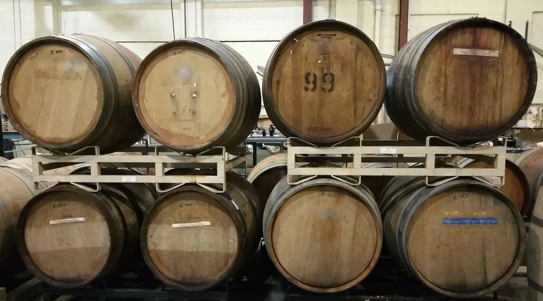 Stacked wooden wine barrels in a cellar, arranged in two rows on metal racks.