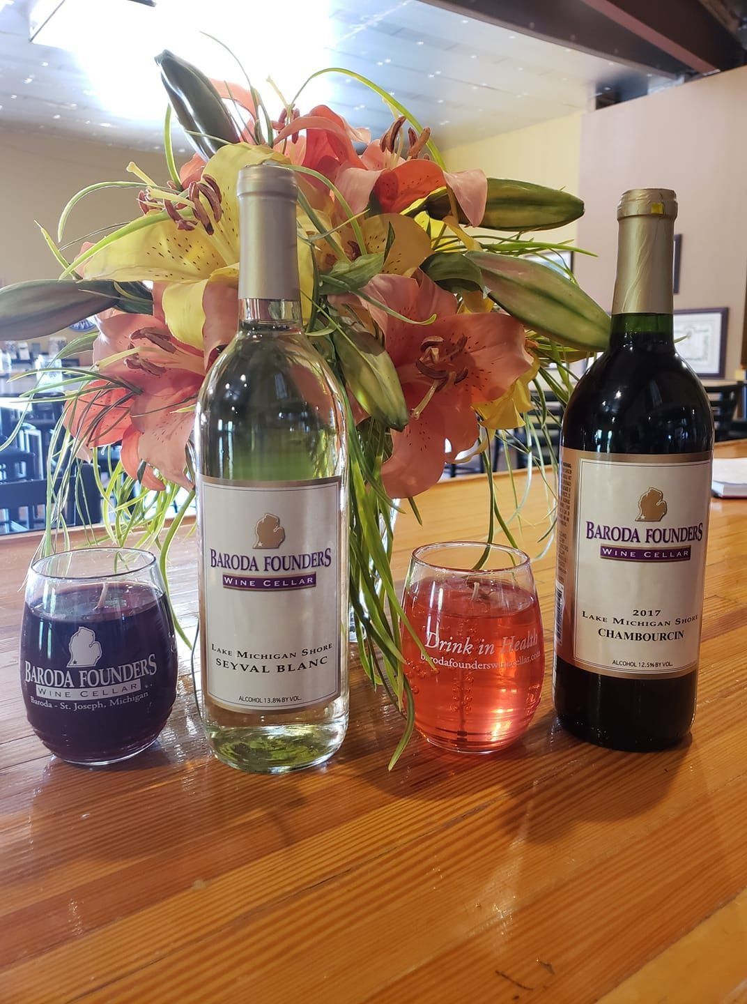 Wine bottles and cocktails on a wooden table with a floral centerpiece in the background