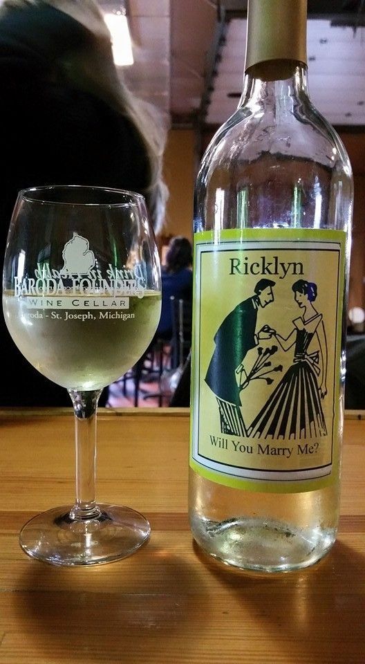 Wine glass and bottle labeled “Ricklyn” on a wooden table, with a blurred person in the background.
