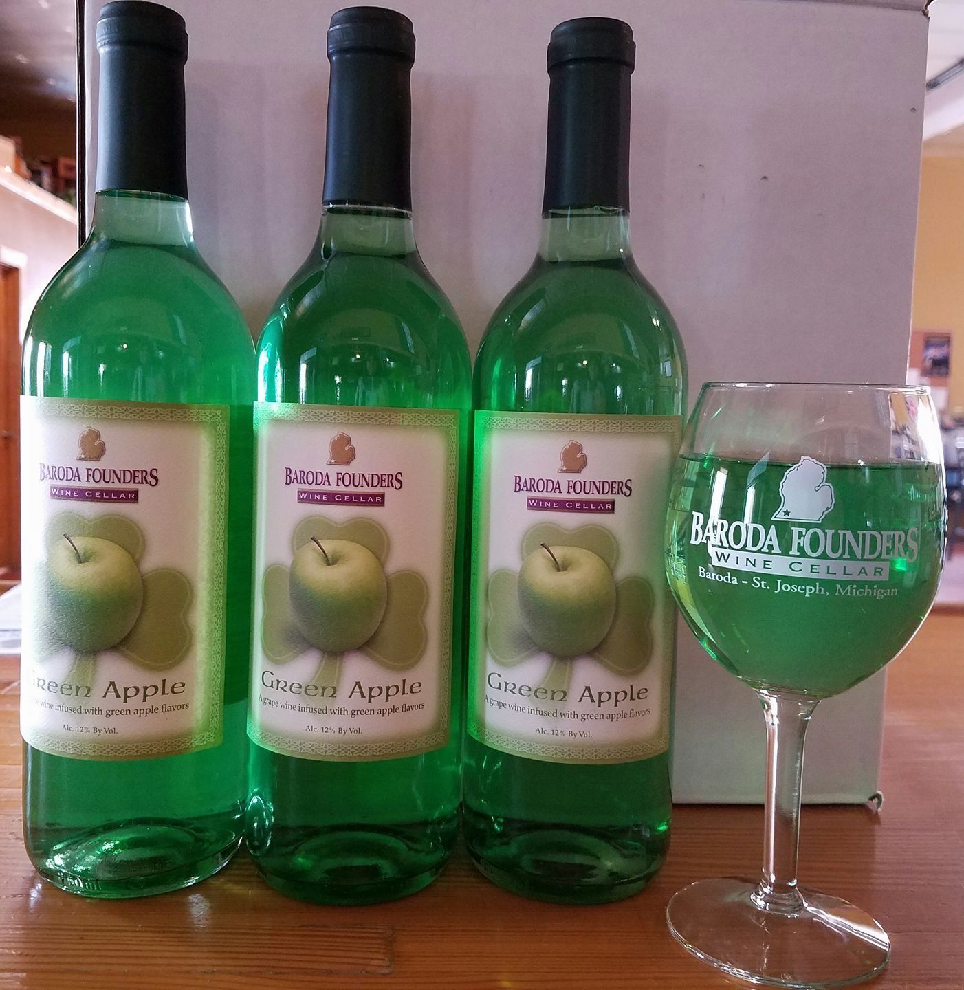Three green apple liqueur bottles beside a green-filled stemmed glass on a countertop.
