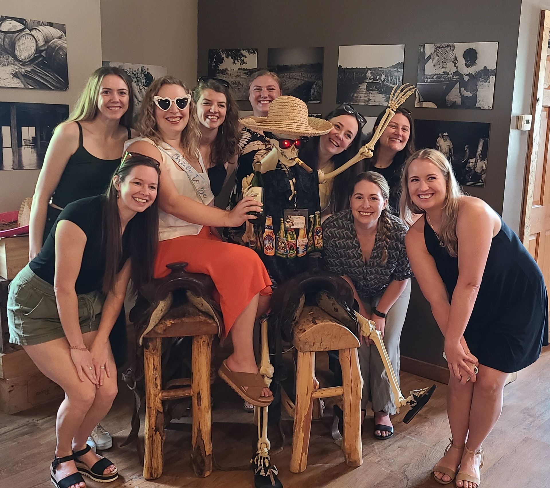 Group of friends posing in a living room with a decorated hat display and wooden stools.