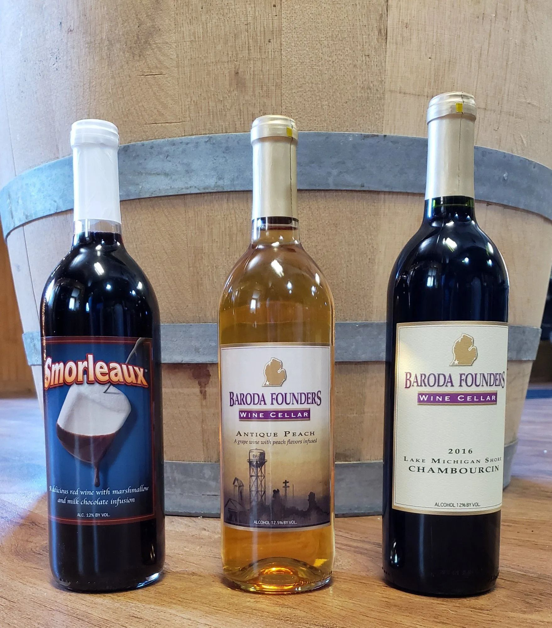 Three wine bottles on a wooden surface, including one red, one white, and one dark red bottle.