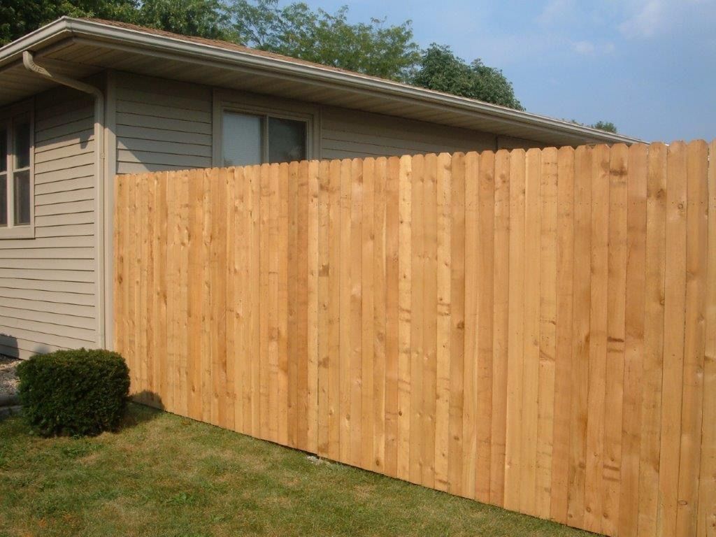 Wooden fence next to a tan house with green grass in the foreground and a blue sky above.