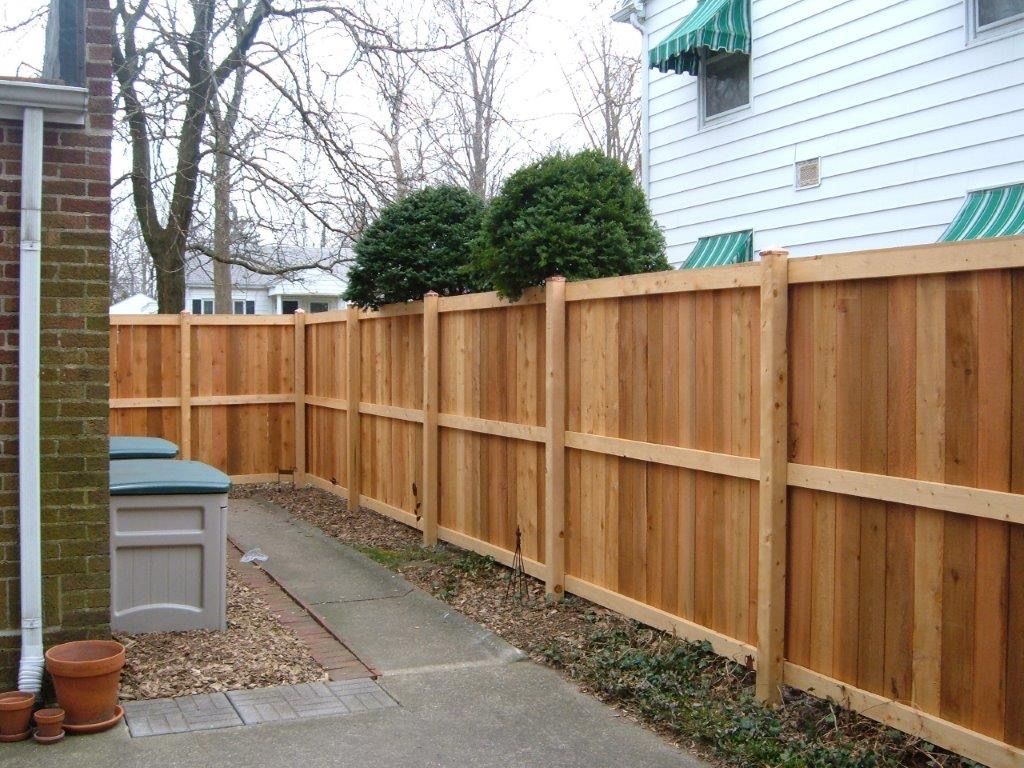 Wooden fence along a concrete path, next to a brick building.