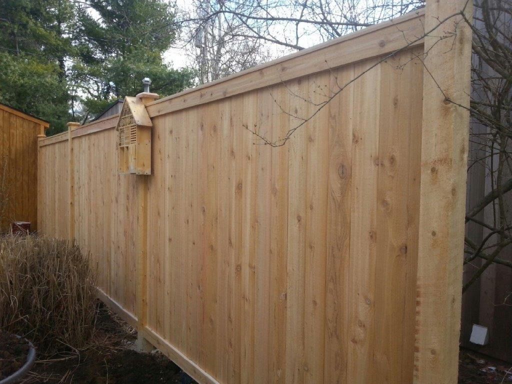 Wooden privacy fence with decorative details, surrounding a yard with greenery.