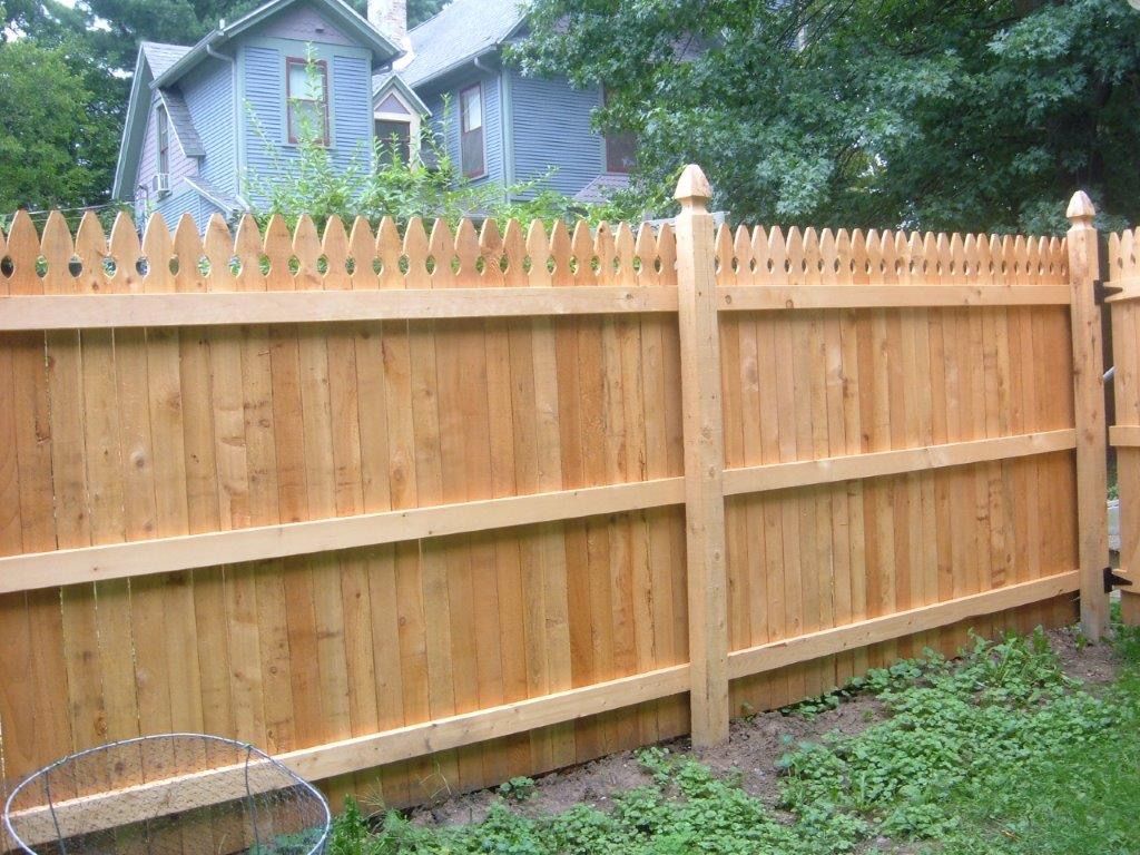 Wooden privacy fence with pointed top, separating a yard from neighborhood houses.