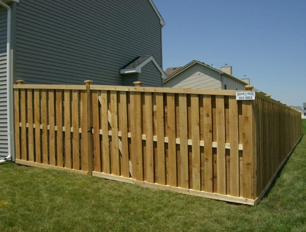 Wooden fence surrounding a grassy yard next to a gray house, sunny day.