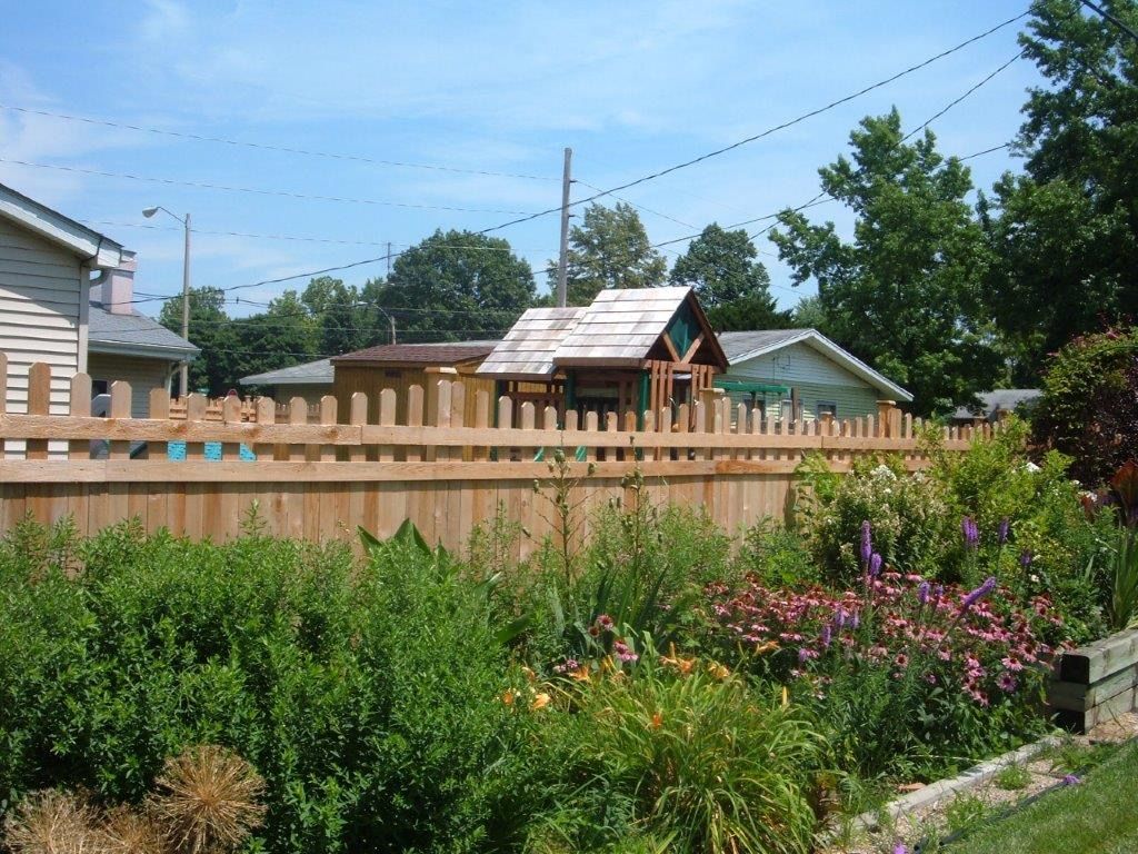 Wooden fence with a garden in front and small playhouse visible in the distance.