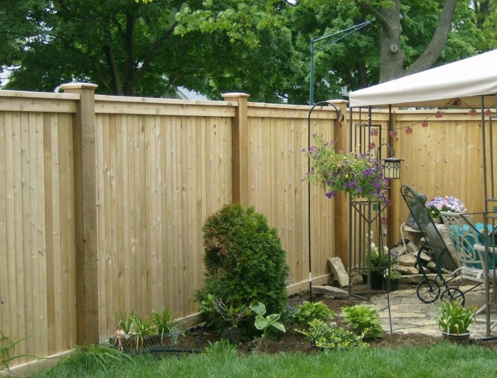 Wooden fence in a backyard with a small garden and patio furniture.