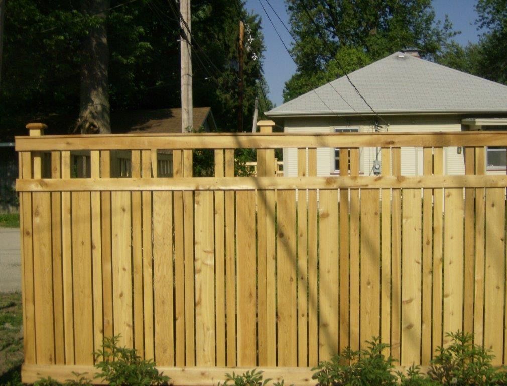 Wooden privacy fence with square cutouts along the top, in front of a house.